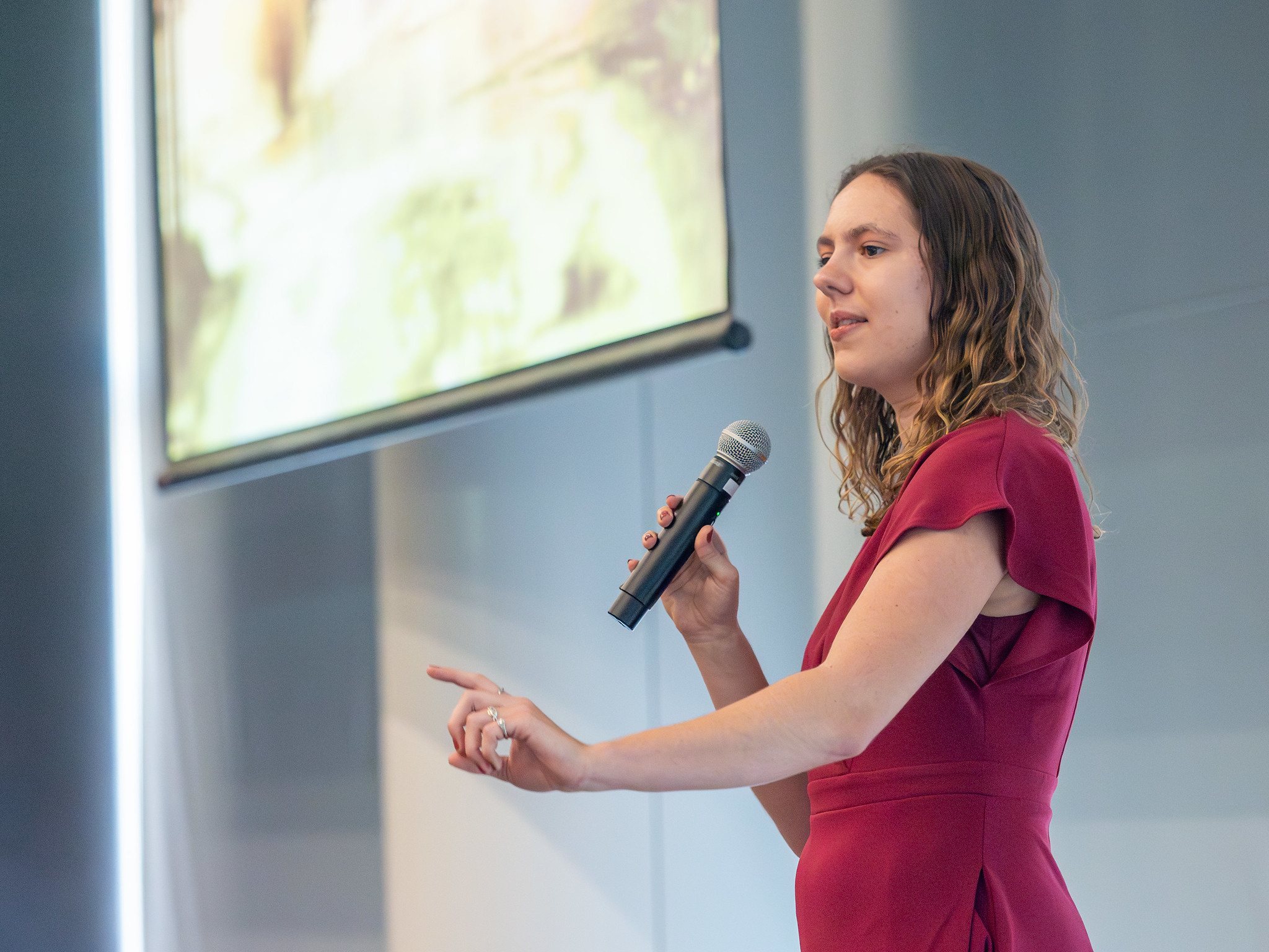 A close-up of Alyssa Griffin mid-presentation. Her arm is extended and she holds a microphone in the other.