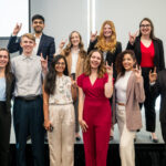 Griffin stands and poses with the 10 finalists. The students make the wolfpack hand symbol with their two middle fingers touching their thumb.