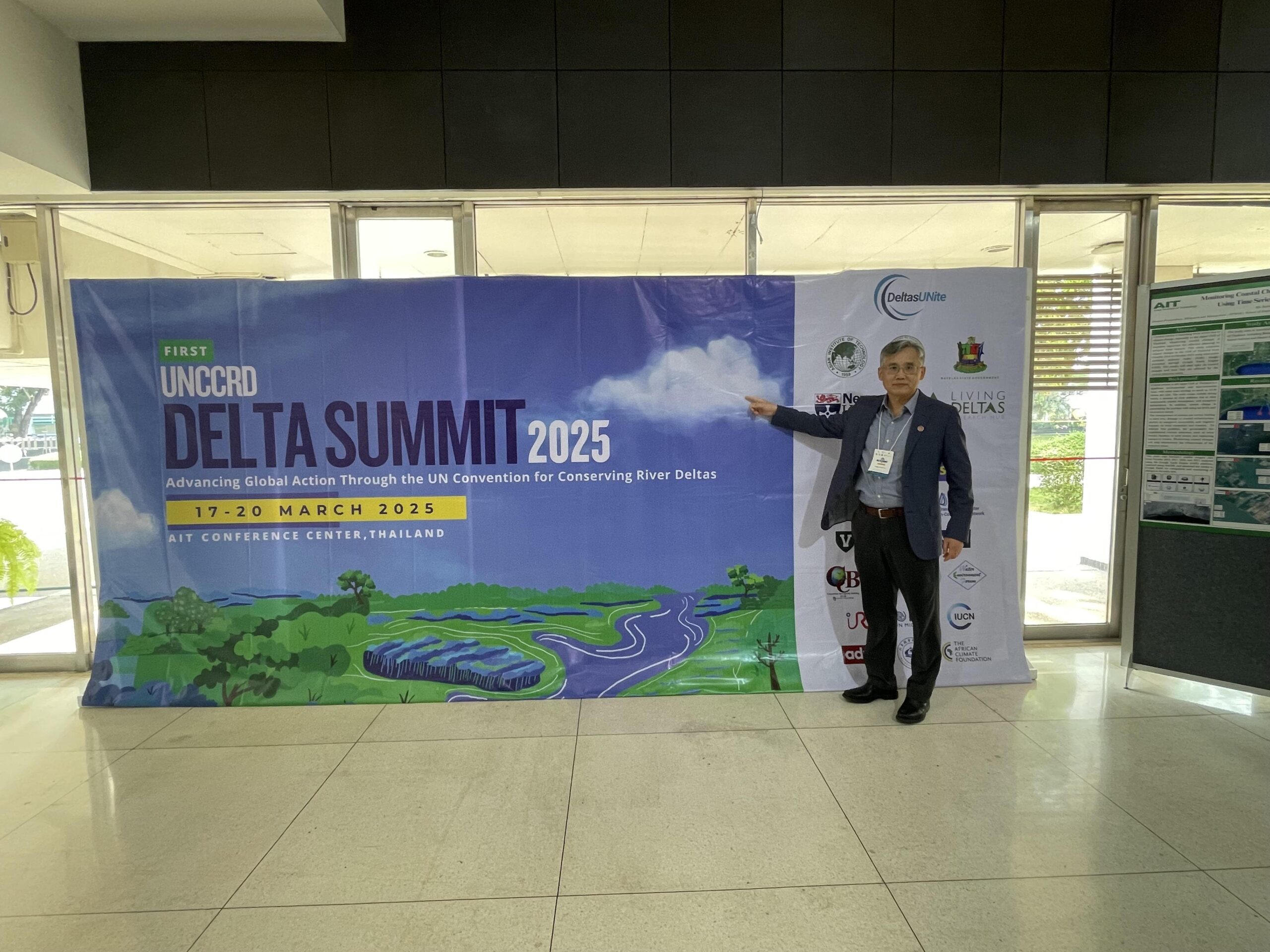 Professor Paul Liu stands beside and points at a banner for the First UNCCRD Delta Summit 2025.