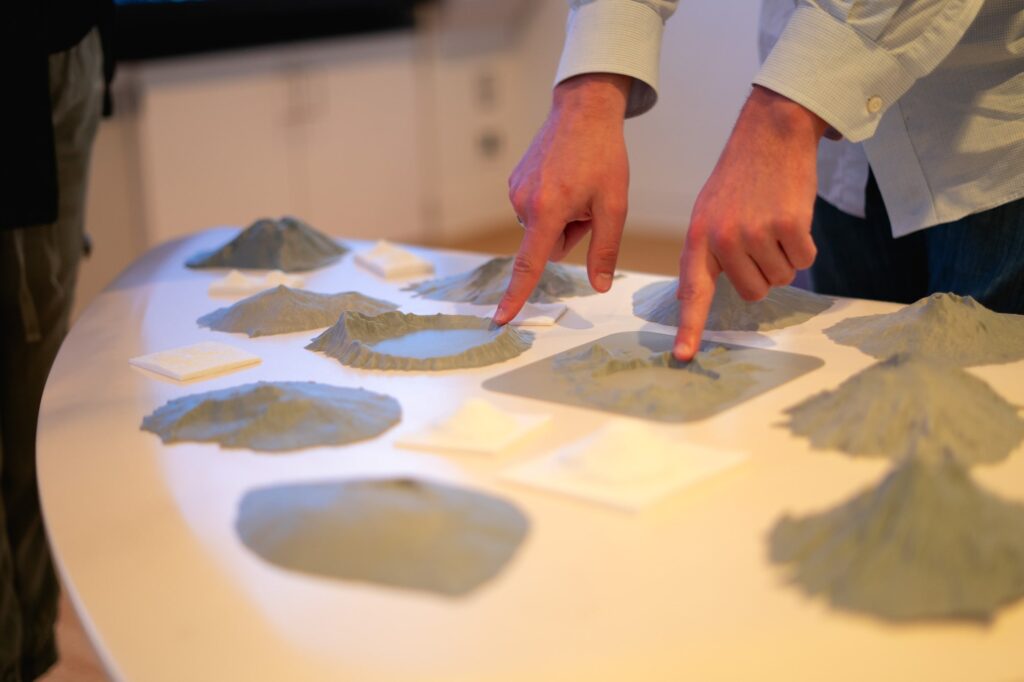 Aiden Nixon points to various features on 3D printed volcanos that sit on a table
