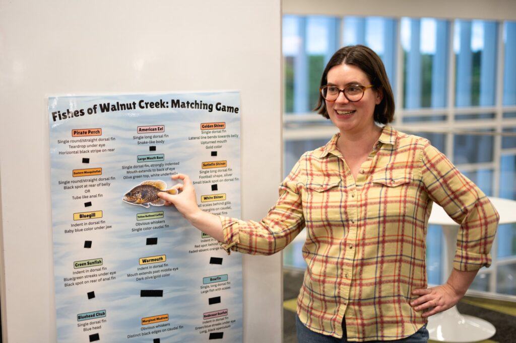 Lily Hughes places a cutout of a fish on a poster, matching the fish to a description of it on the poster, which is a matching game
