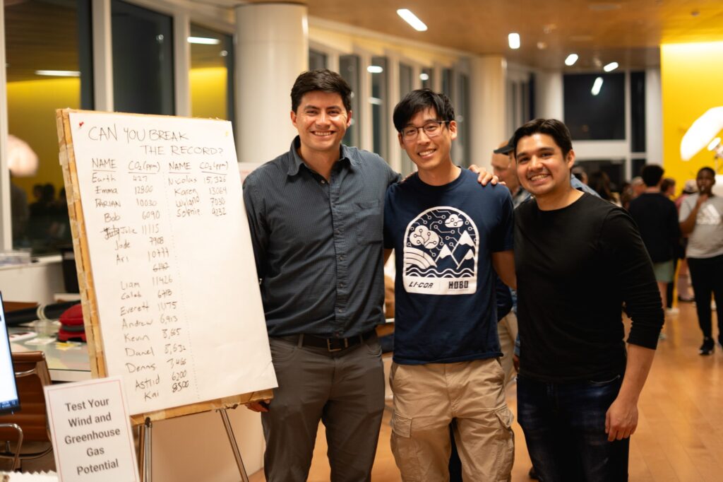 Professor Camilo Rey-Sanchez and students Sebastian Emilio Diaz Cortes and Darian Ng pose together in front of a poster where they recorded people's scores from their activity