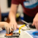 A child's hand is in focus, playing with a lego crane machine