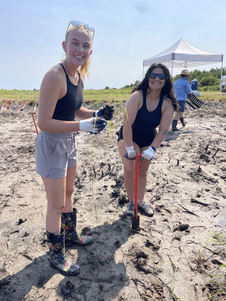 Two students smiling while holding an orange dibble bar and plant plug