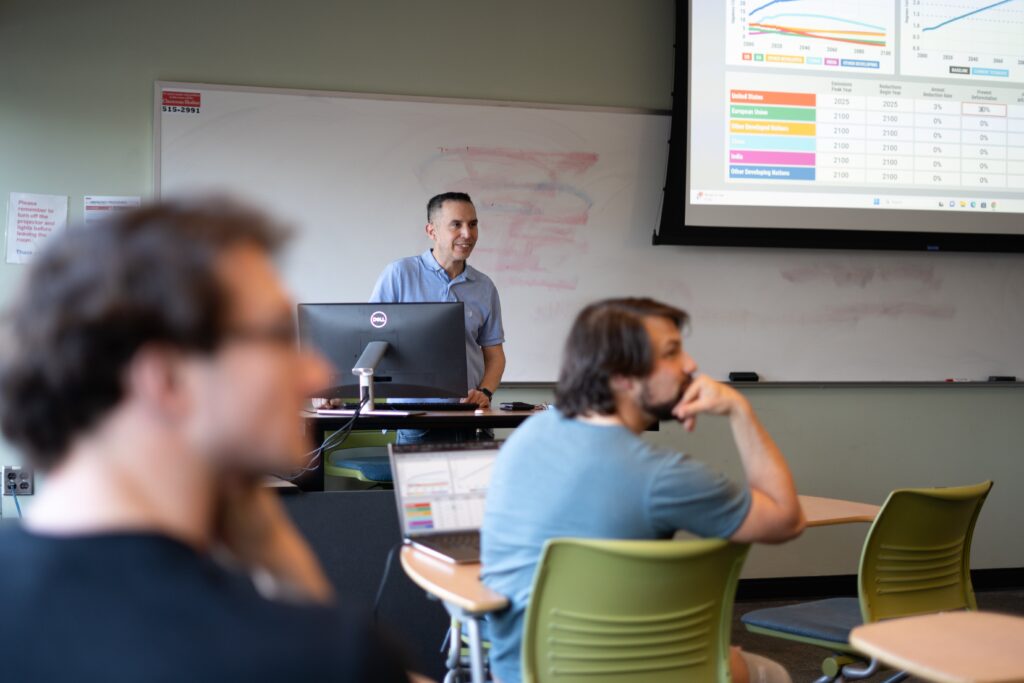 Mera stands at the front of a classroom, with students engaged in discussion