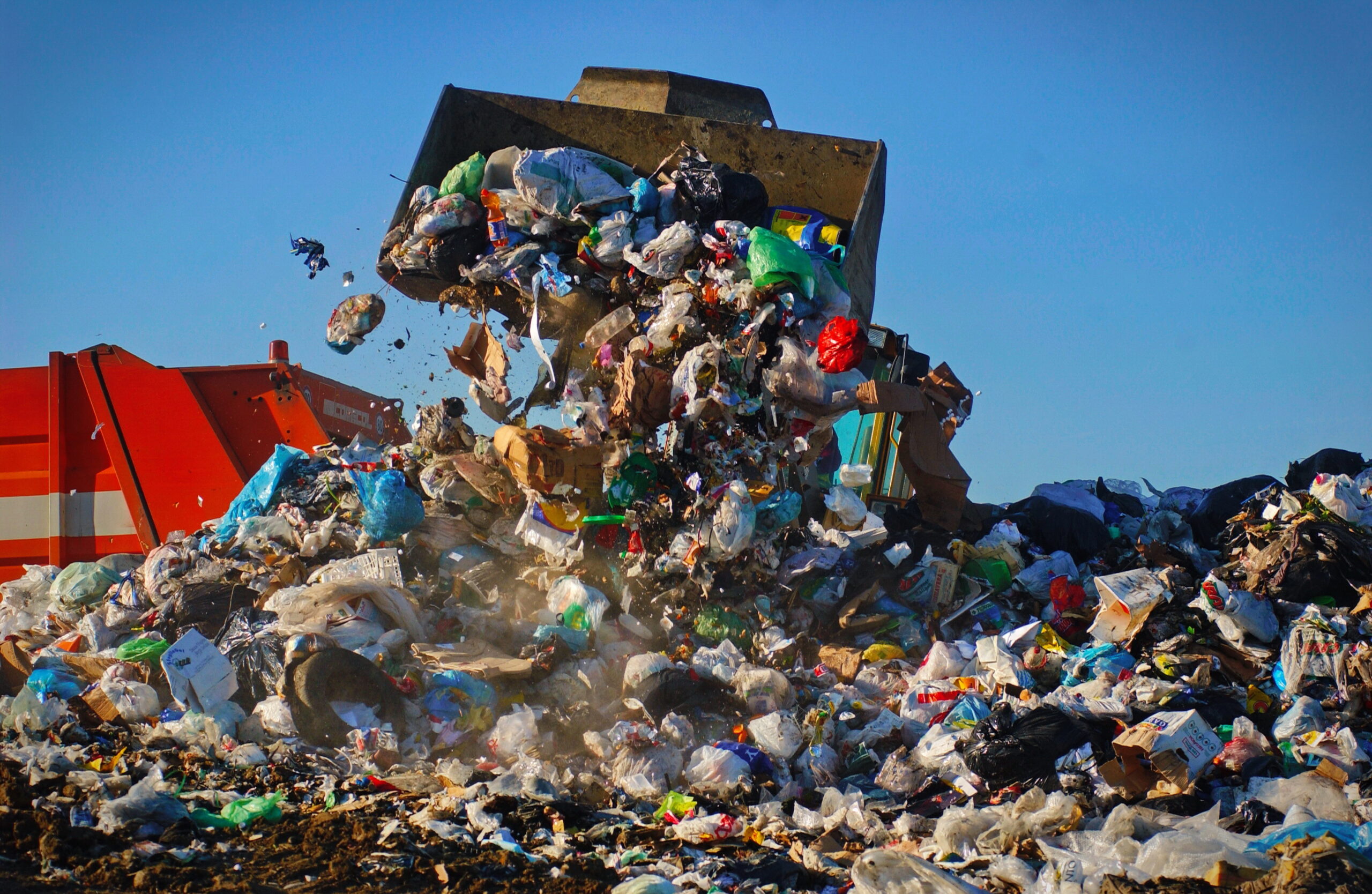A garbage truck tossing bags of trash into a landfill