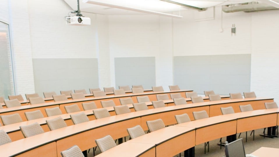 a large, conference-style classroom with rows of tan chairs and tables